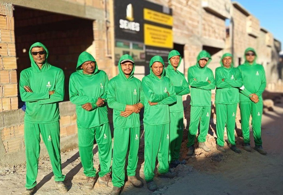 Integrantes da equipe SENEG Construções com uniformes verdes em frente a uma obra